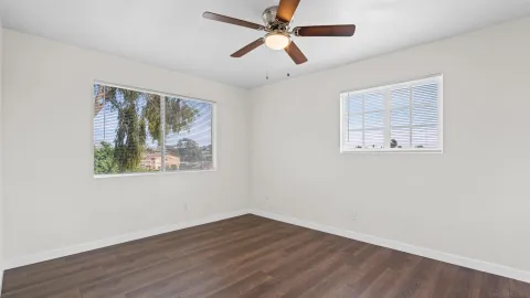 a view of an empty room with wooden floor and a ceiling fan