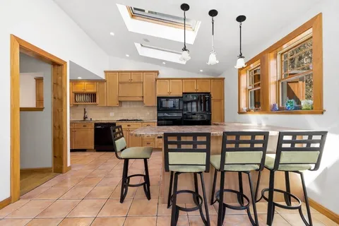 a kitchen with stainless steel appliances granite countertop a stove top oven a refrigerator a sink and chairs