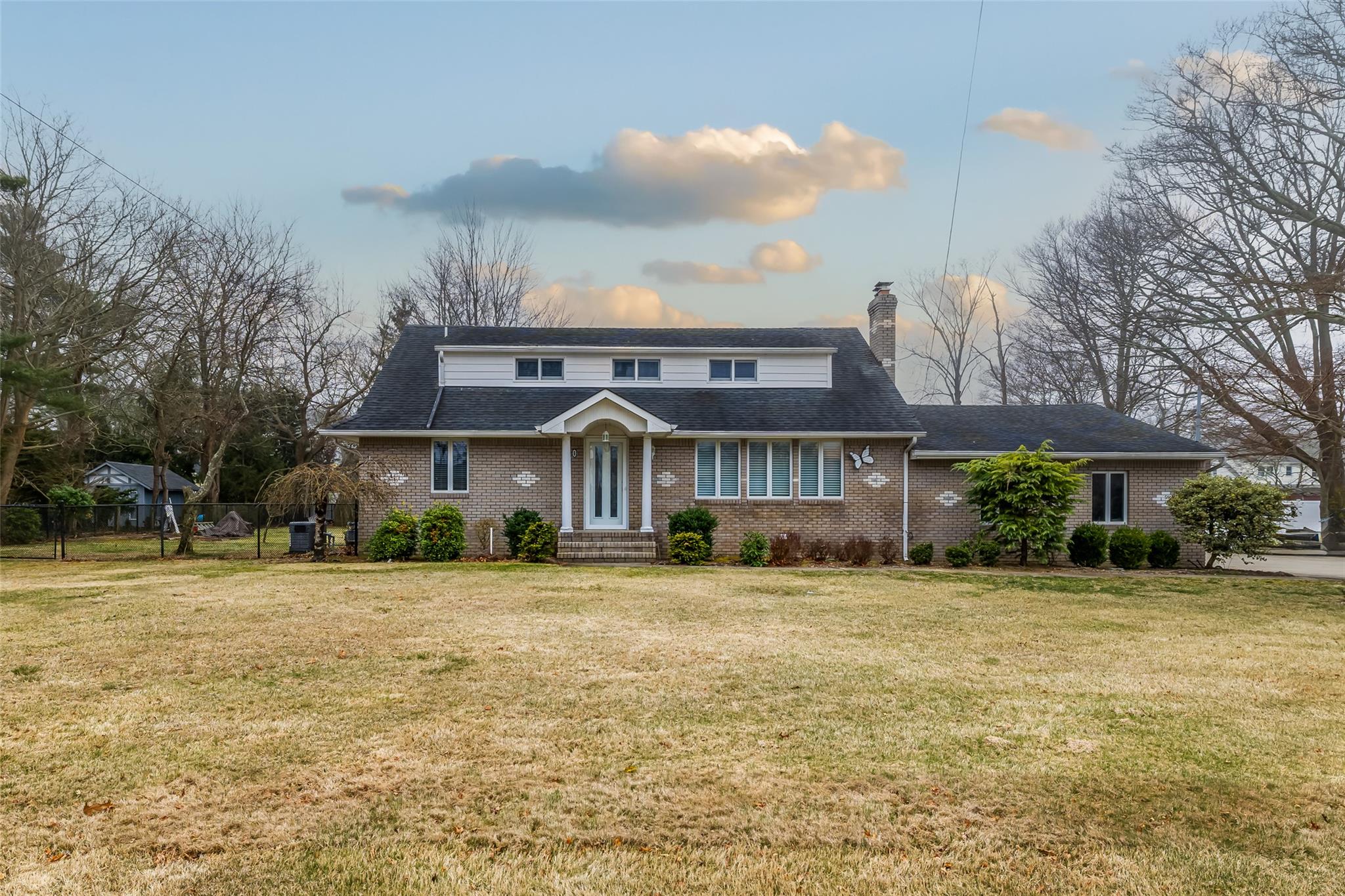 Traditional-style home with brick siding, fence, a chimney, and a front yard
