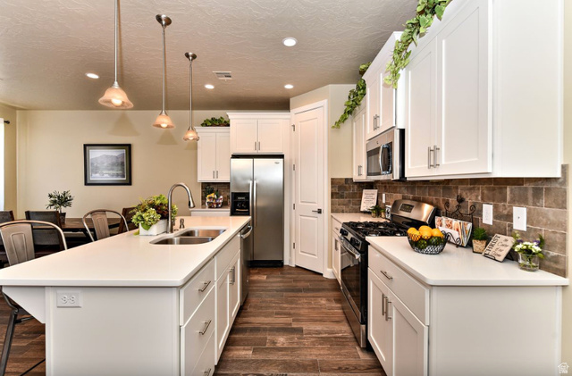 1622 Canyon Tree Drive St. George, UT 84770 - Photo 2 of 34 Contemporary kitchen featuring an expansive center island with an undermount double sink, white cabinetry, stainless steel appliances, a tile backsplash, and wood-finish flooring