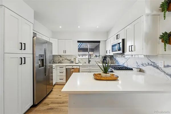 a kitchen with kitchen island a refrigerator a stove a oven a sink dishwasher and white cabinets with wooden floor