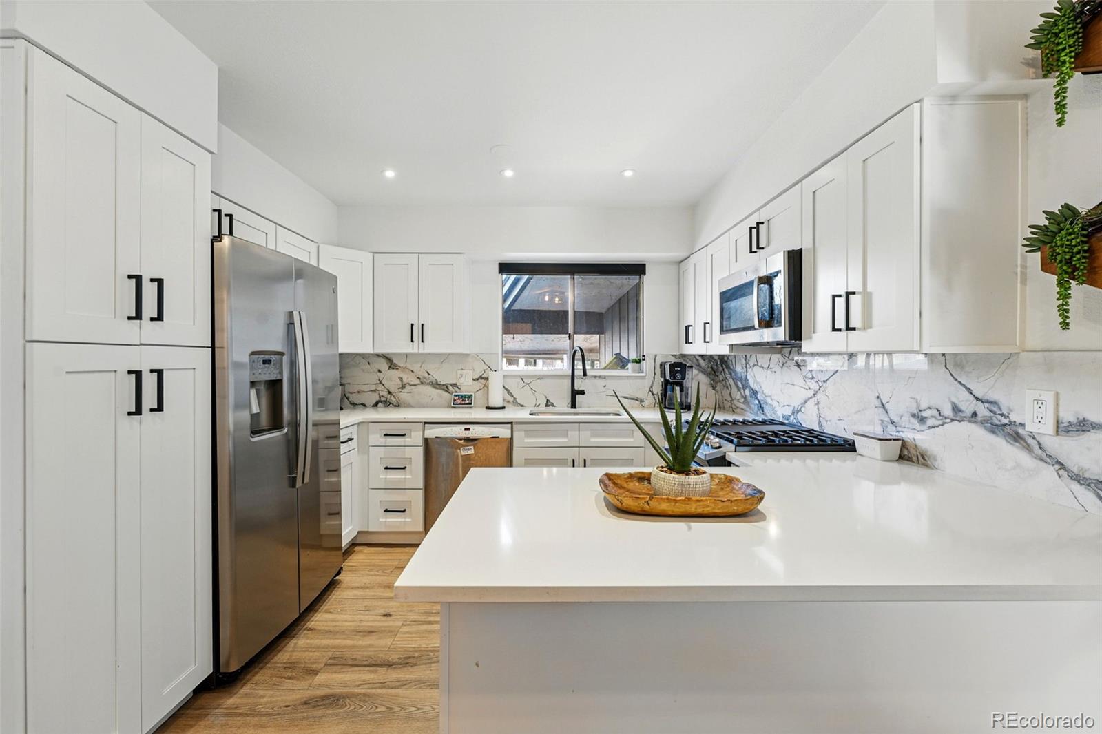 a kitchen with kitchen island a refrigerator a stove a oven a sink dishwasher and white cabinets with wooden floor