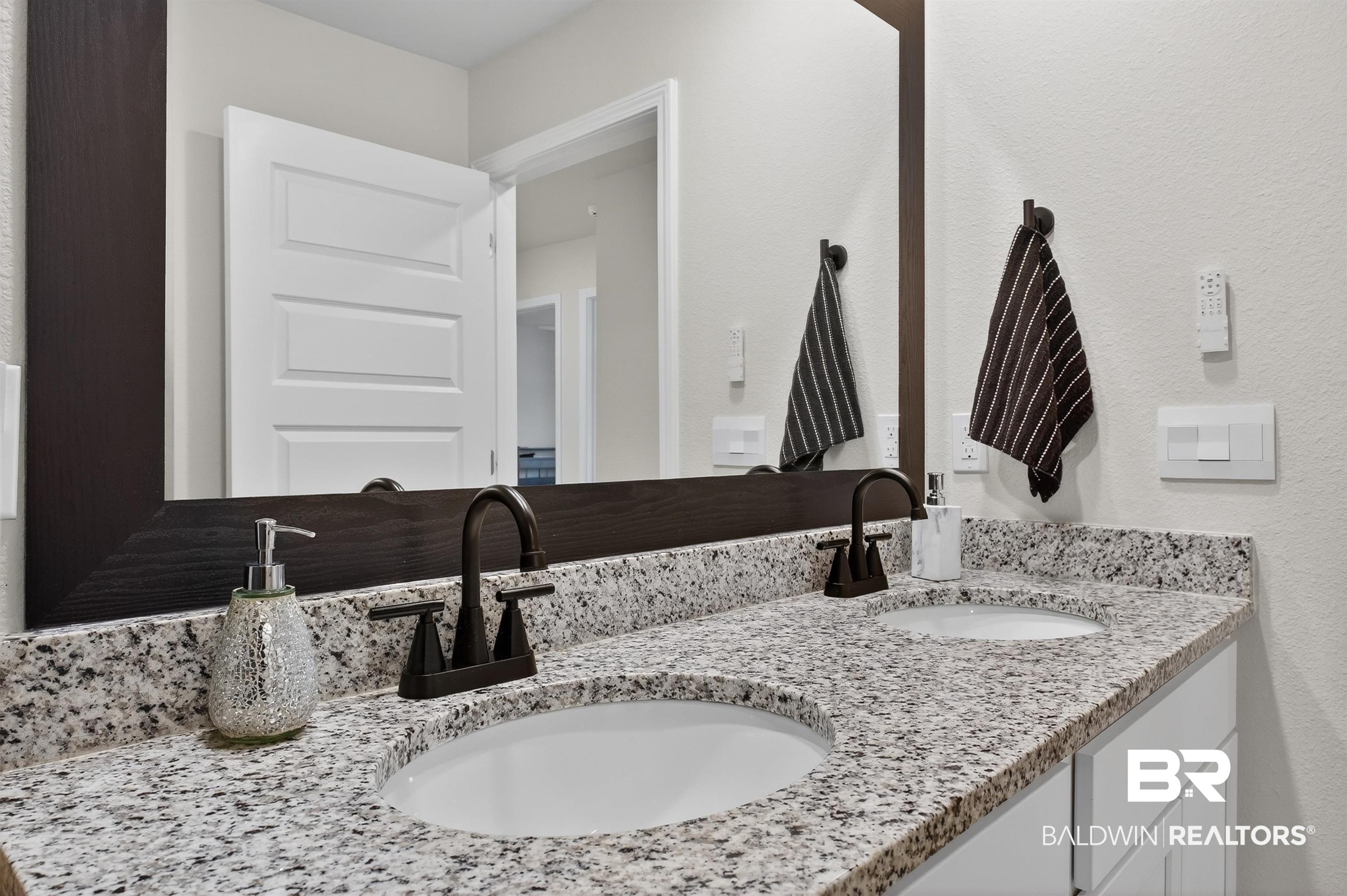3213 Camino Real Loop Lillian, AL 36549 - Photo 53 of 61 Dual vanity with white undermount sinks, speckled stone countertop, dark bronze faucets, and a framed mirror
