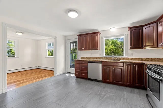 a kitchen with stainless steel appliances granite countertop wooden cabinets a sink a stove a window and wooden floors