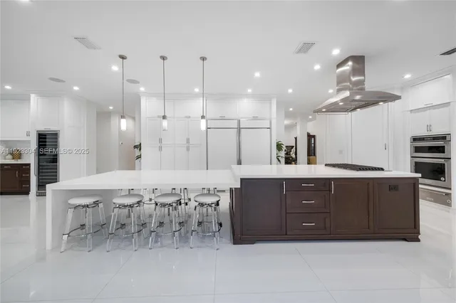 a large white kitchen with stainless steel appliances granite countertop a stove a sink a refrigerator and white cabinets with wooden floor