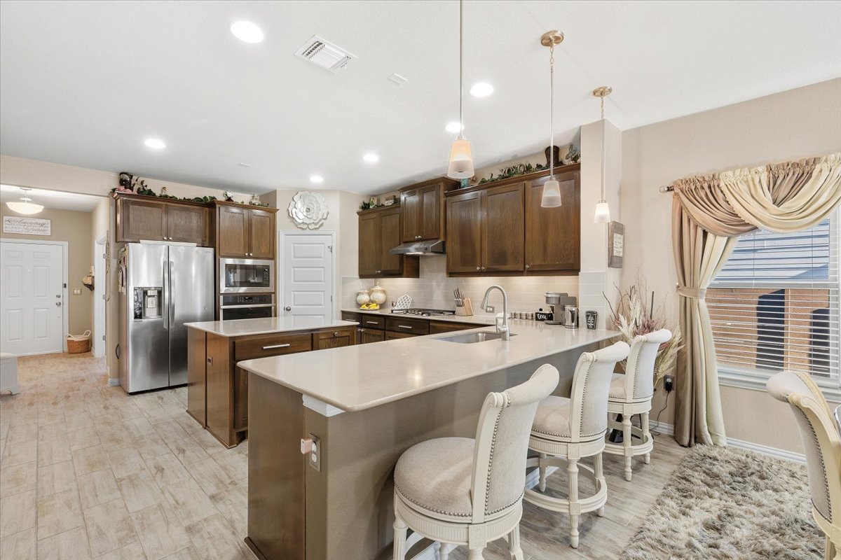 8721 Sikes Way Austin, TX 78747 - Photo 8 of 37 Kitchen featuring a center island, a peninsula, a kitchen bar, stainless steel appliances, and light wood finished floors