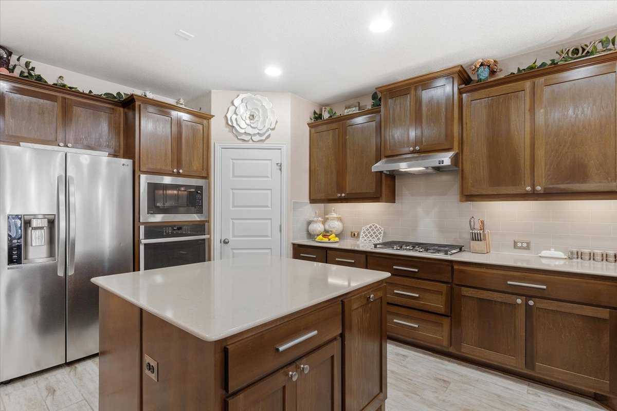 8721 Sikes Way Austin, TX 78747 - Photo 9 of 37 Kitchen with stainless steel appliances, decorative backsplash, a kitchen island, light stone countertops, and recessed lighting