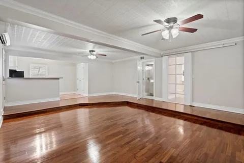 a view of an empty room with wooden floor and a ceiling fan