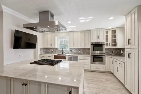a kitchen with stainless steel appliances kitchen island granite countertop a refrigerator oven a sink dishwasher and white cabinets with wooden floor