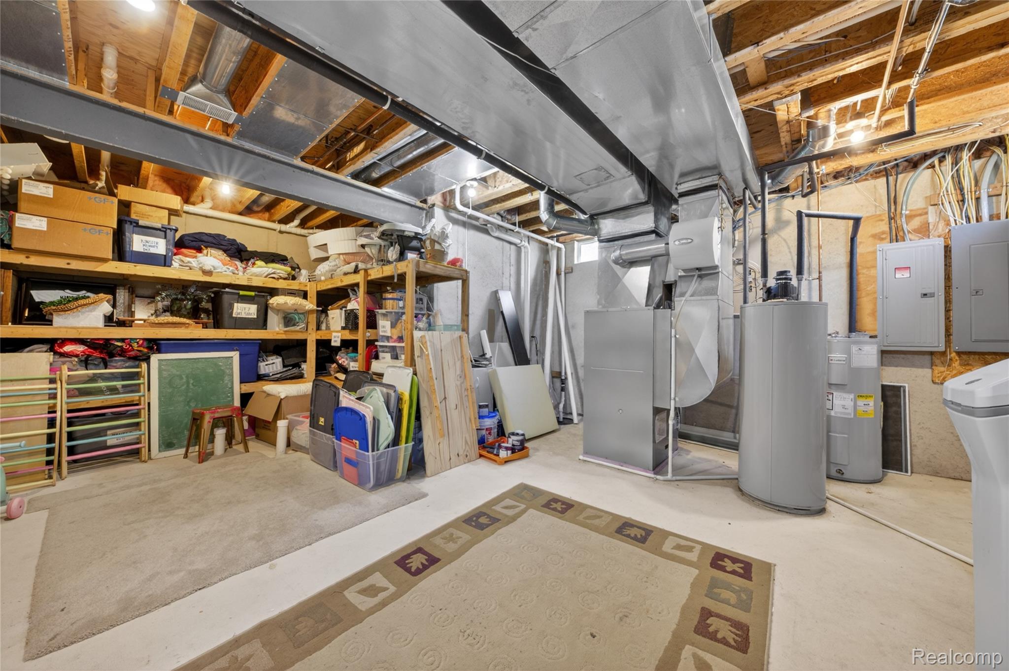 9191 Judd Road Fowlerville, MI 48836 - Photo 60 of 74 Unfinished basement space featuring exposed wood joists and structural beams, concrete flooring, water heater, furnace, and electrical panels