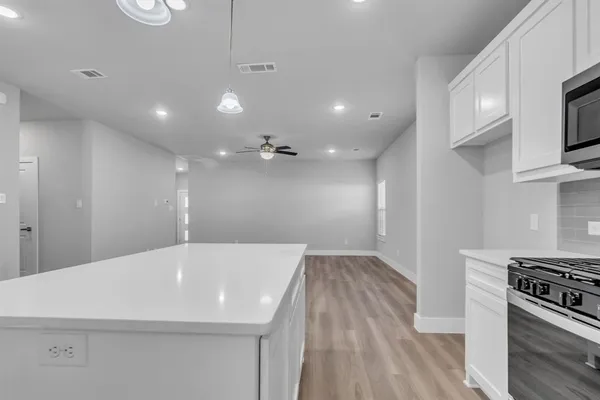 a large kitchen with kitchen island a stove a sink a refrigerator white cabinets and wooden floor