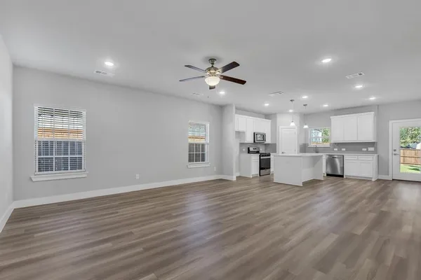 a view of an empty room with wooden floor and a kitchen