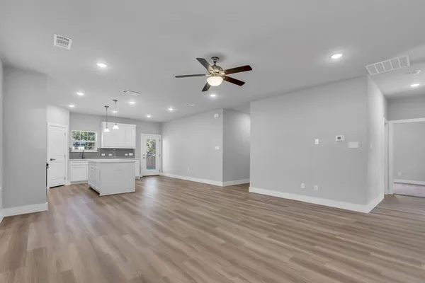 a view of an empty room and kitchen with wooden floor