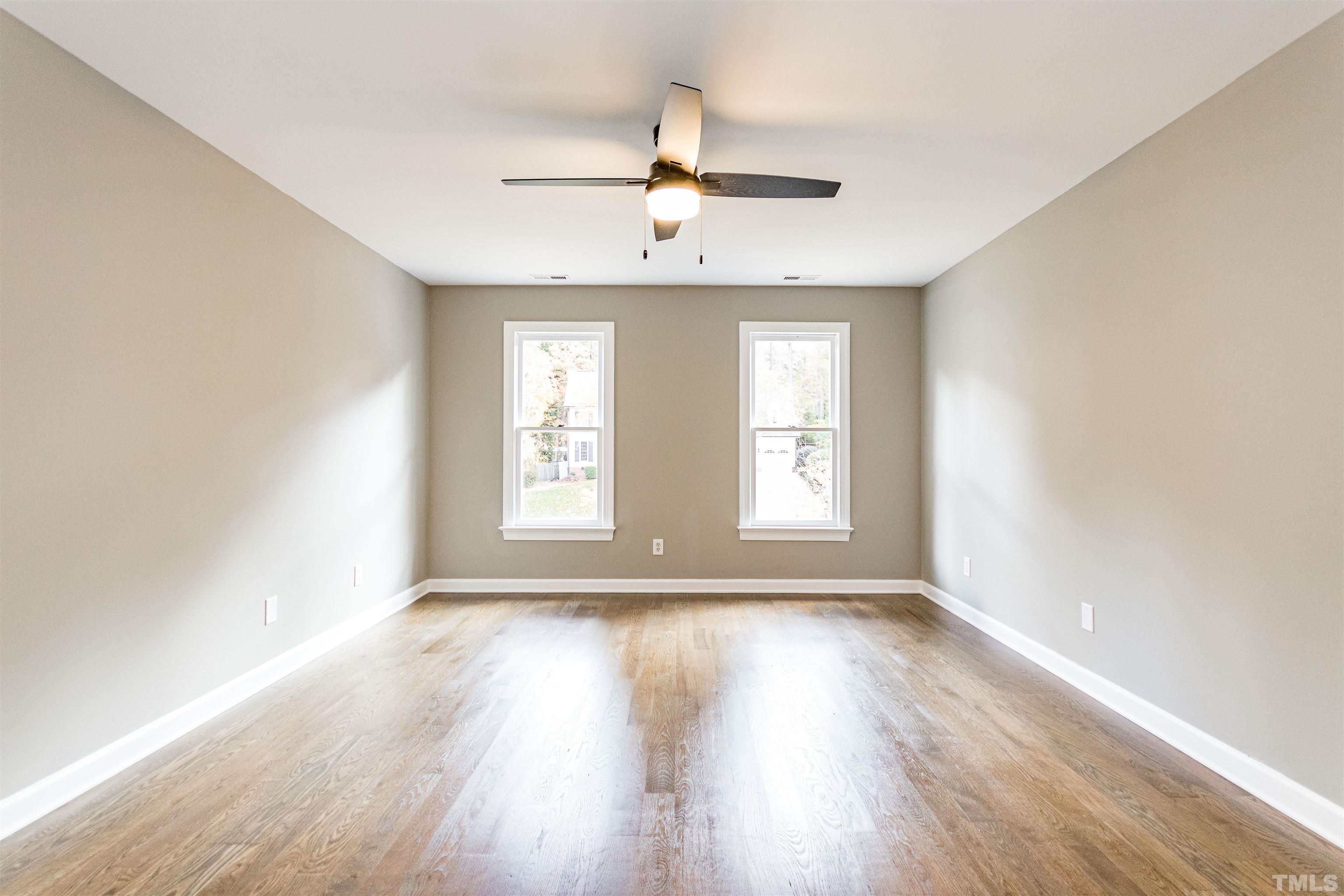 8105 Laurel Mountain Road Raleigh, NC 27613 - Photo 12 of 26 an empty room with wooden floor windows and ceiling fan