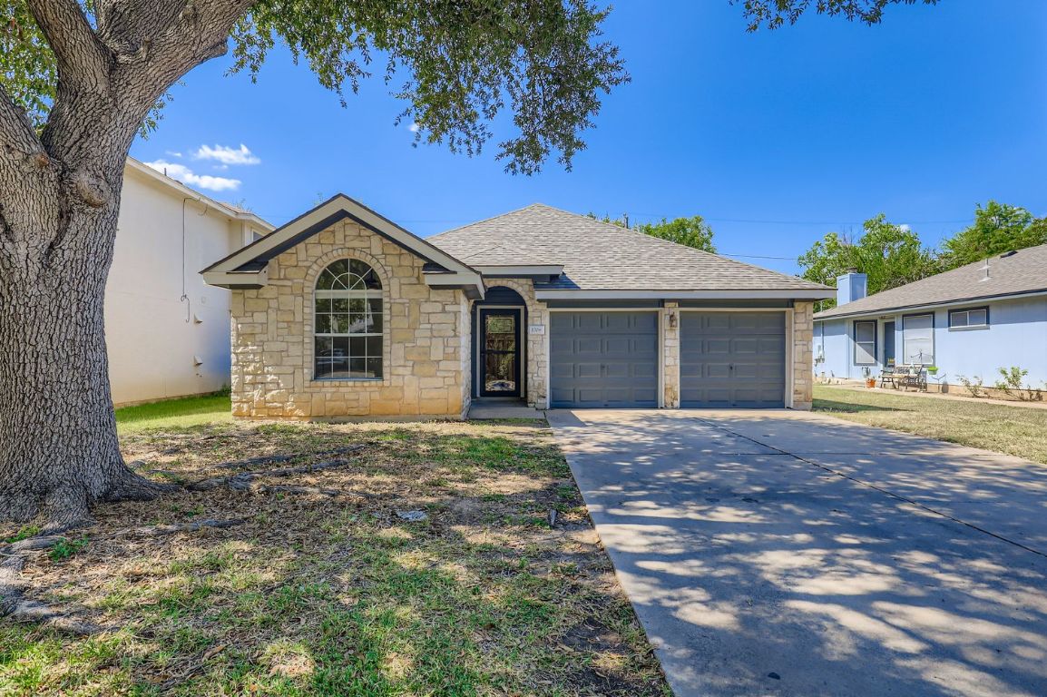 View of front of home featuring stone siding, an attached garage, driveway, and a shingled roof