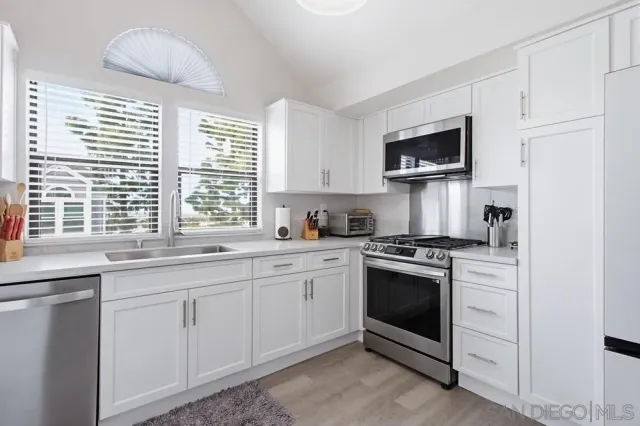 a kitchen with stainless steel appliances granite countertop white cabinets a sink and a window