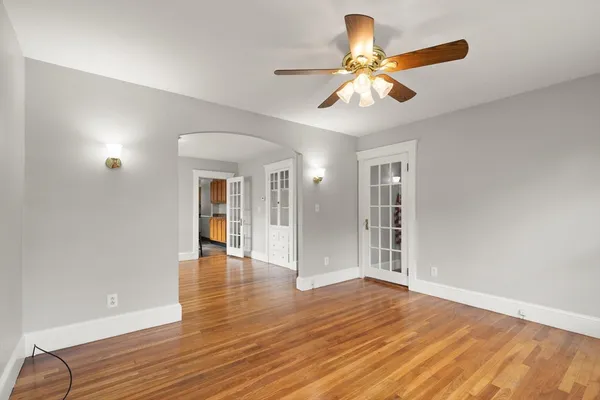 a view of an empty room with wooden floor and a ceiling fan