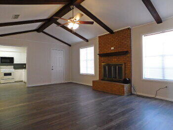 4422 57th Street Lubbock, TX 79414 - Photo 2 of 19 an empty room with wooden floor a ceiling fan a fireplace and windows