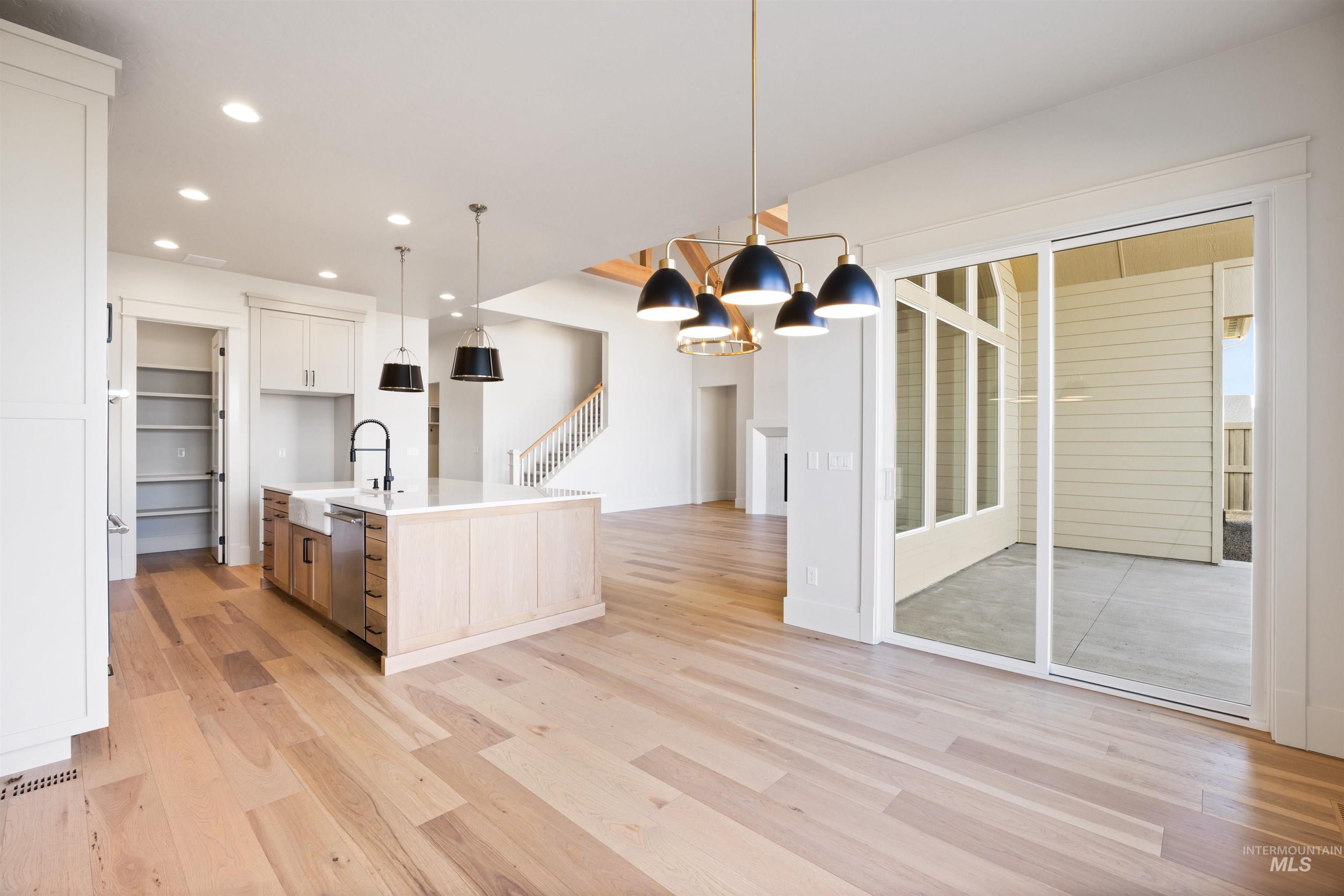1090 East Crescendo Street Meridian, ID 83642 - Photo 13 of 50 Dual tone kitchen featuring a center island with sink, hanging lights, light wood-style flooring, two tone color scheme, and light stone counters