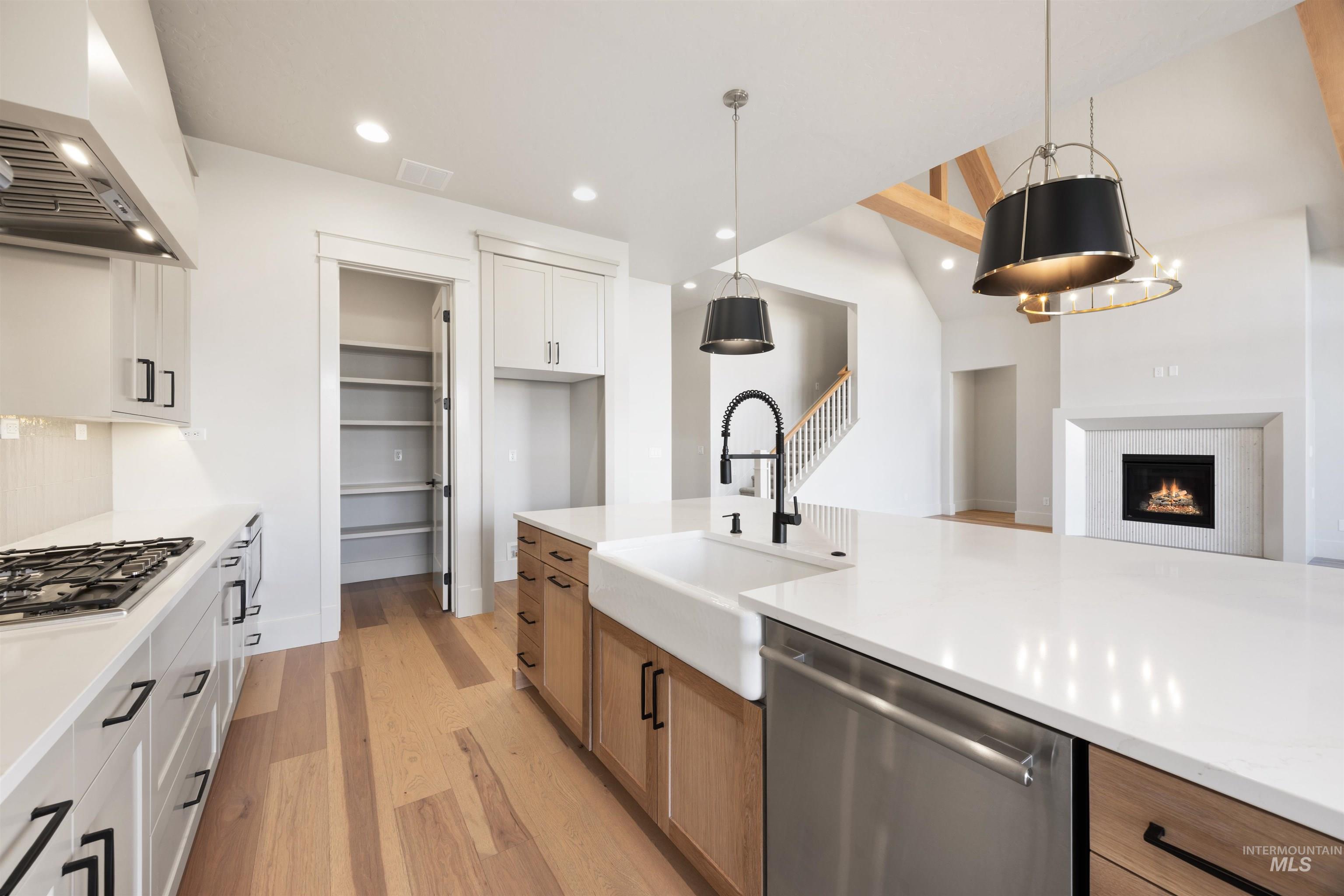 1090 East Crescendo Street Meridian, ID 83642 - Photo 16 of 50 Kitchen featuring two tone cabinets, stainless steel appliances, light wood finished floors, hanging light fixtures, and a warm lit fireplace