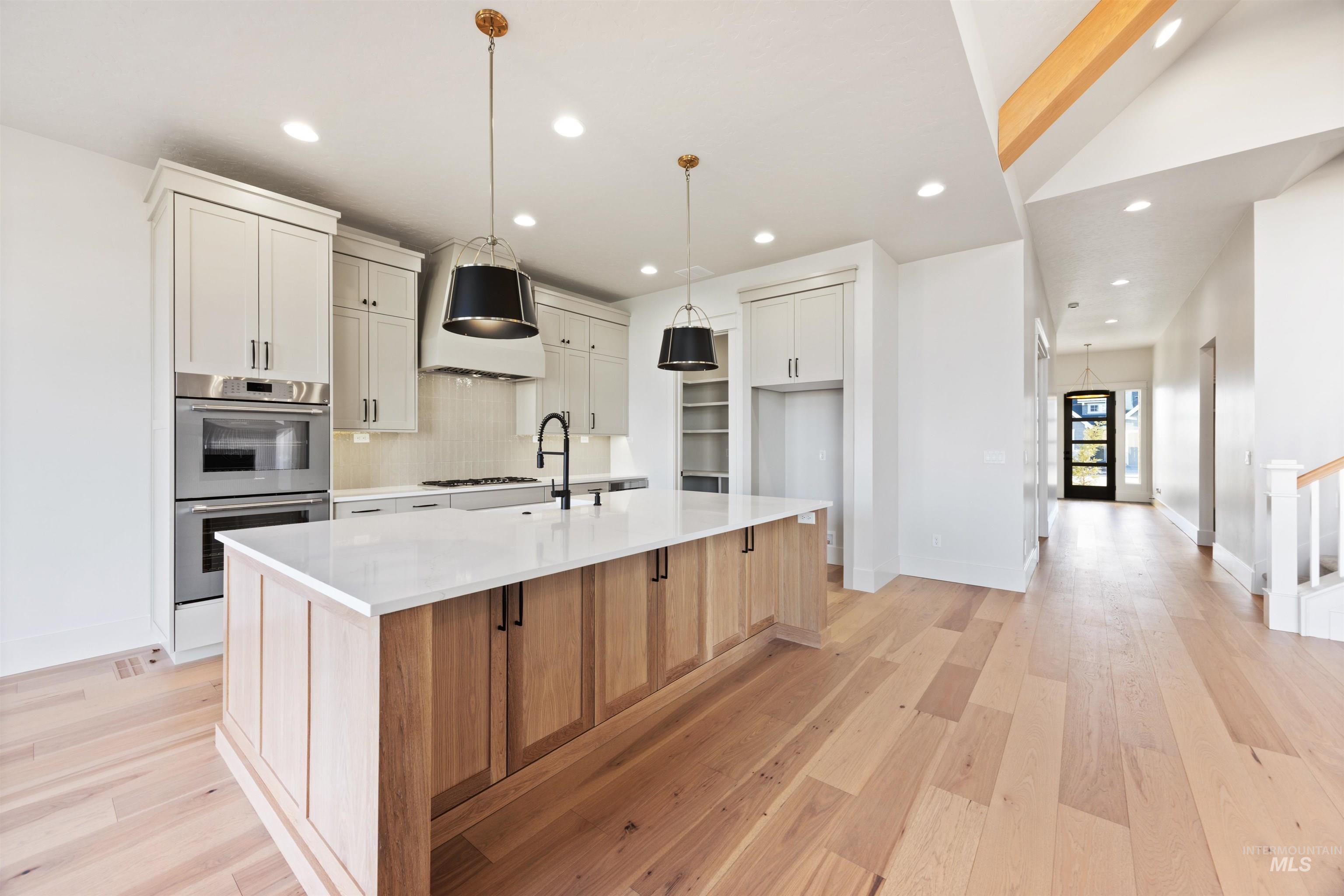 1090 East Crescendo Street Meridian, ID 83642 - Photo 17 of 50 Kitchen featuring two tone cabinets, double oven, light wood-style floors, hanging light fixtures, and a center island with sink