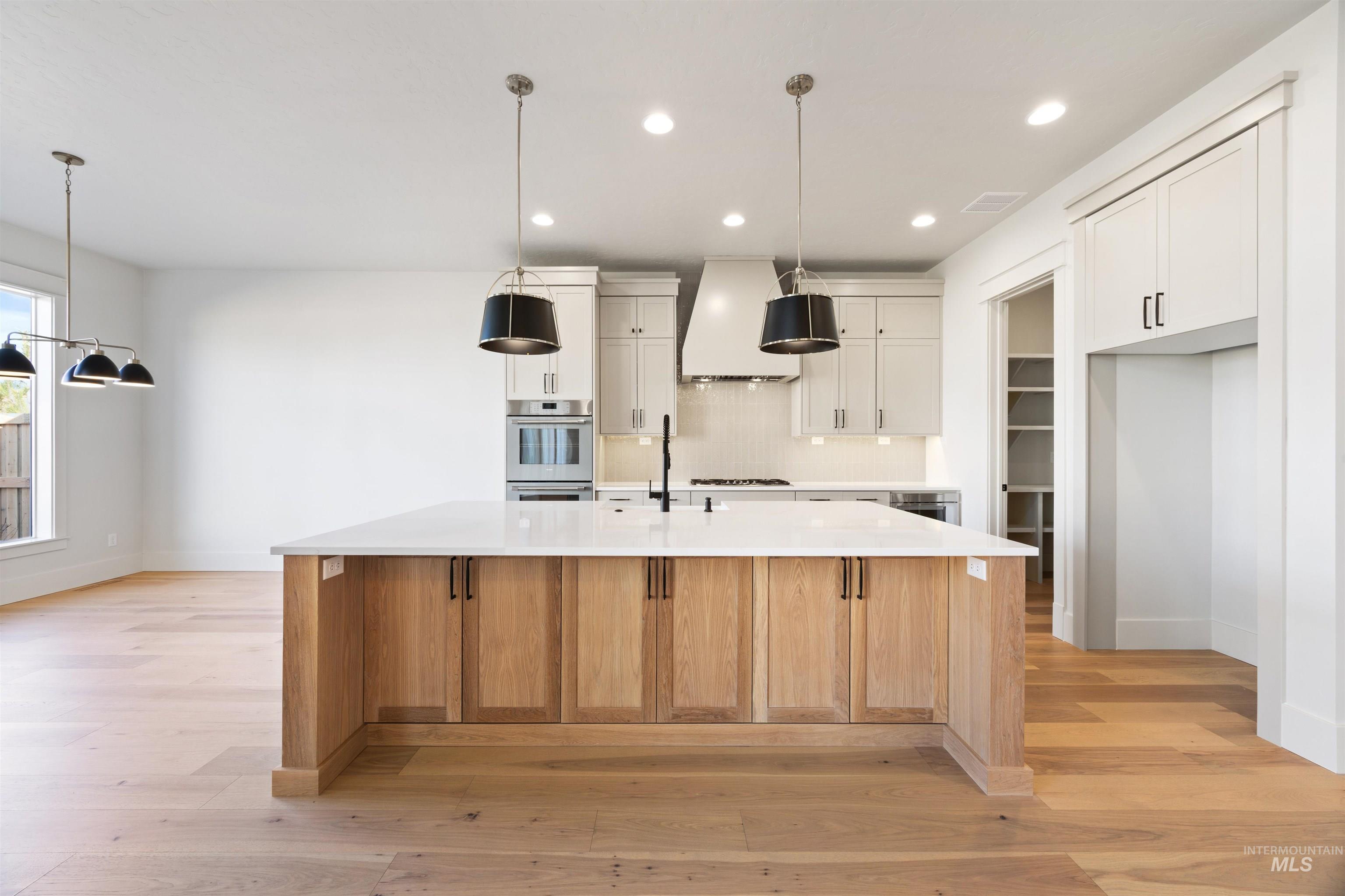 1090 East Crescendo Street Meridian, ID 83642 - Photo 19 of 50 Dual tone kitchen featuring two tone cabinets, light wood-type flooring, pendant lighting, a spacious island, and light stone countertops