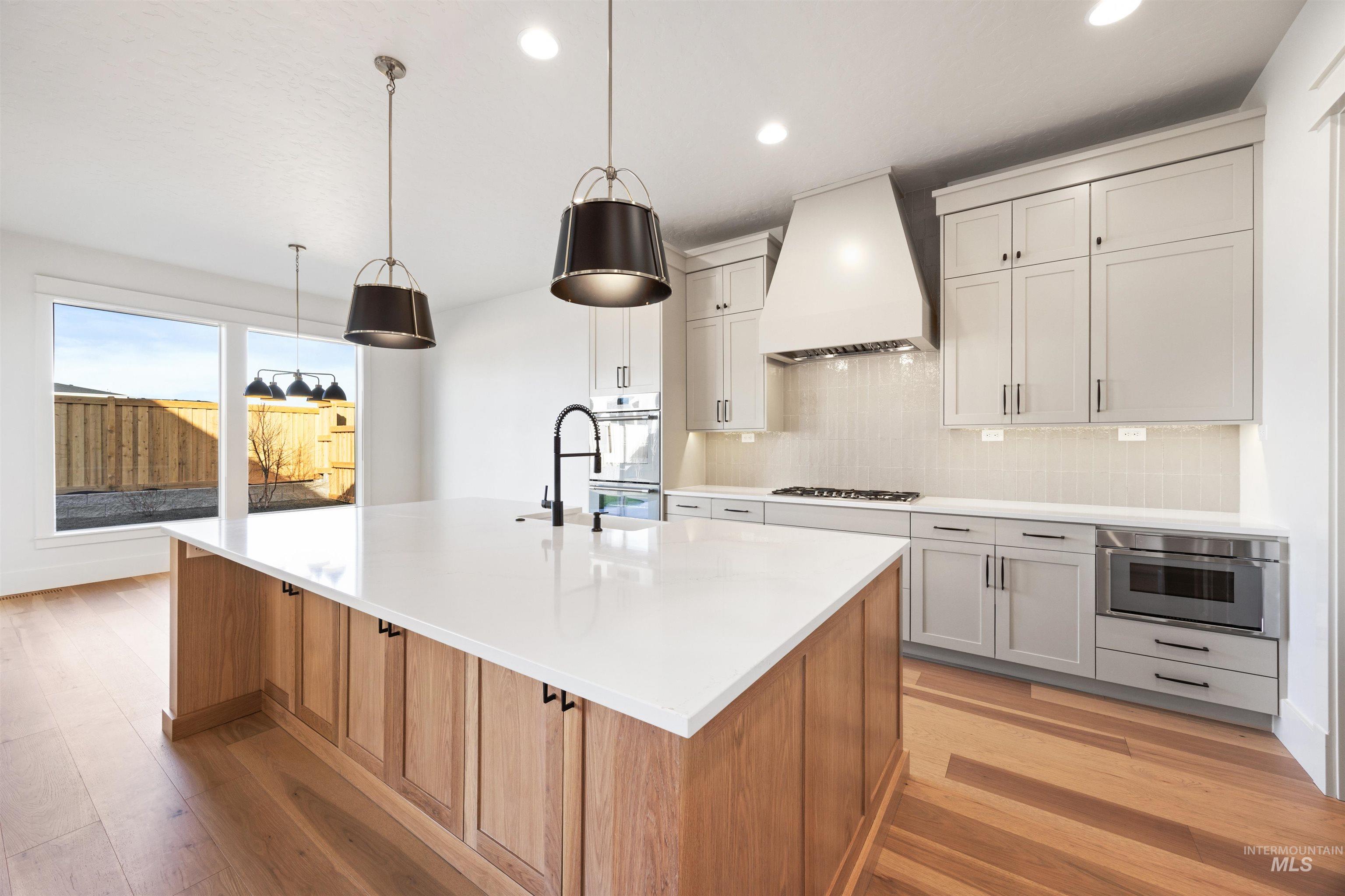 1090 East Crescendo Street Meridian, ID 83642 - Photo 21 of 50 Kitchen with tasteful backsplash, two tone cabinetry, light wood-style floors, a center island with sink, and pendant lighting
