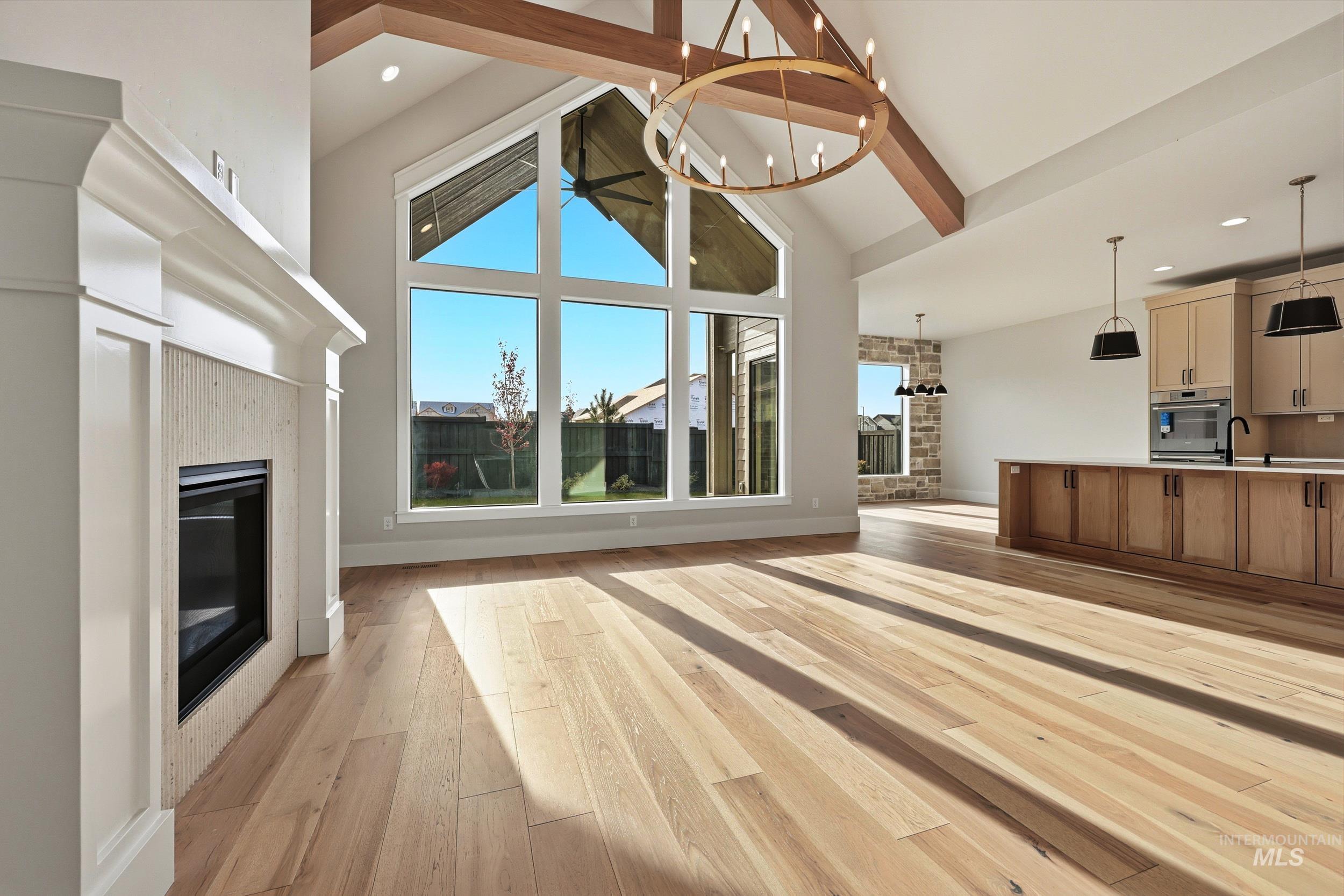 1090 East Crescendo Street Meridian, ID 83642 - Photo 3 of 43 Unfurnished living room featuring a glass covered fireplace, beamed ceiling, light wood-style floors, a chandelier, and high vaulted ceiling