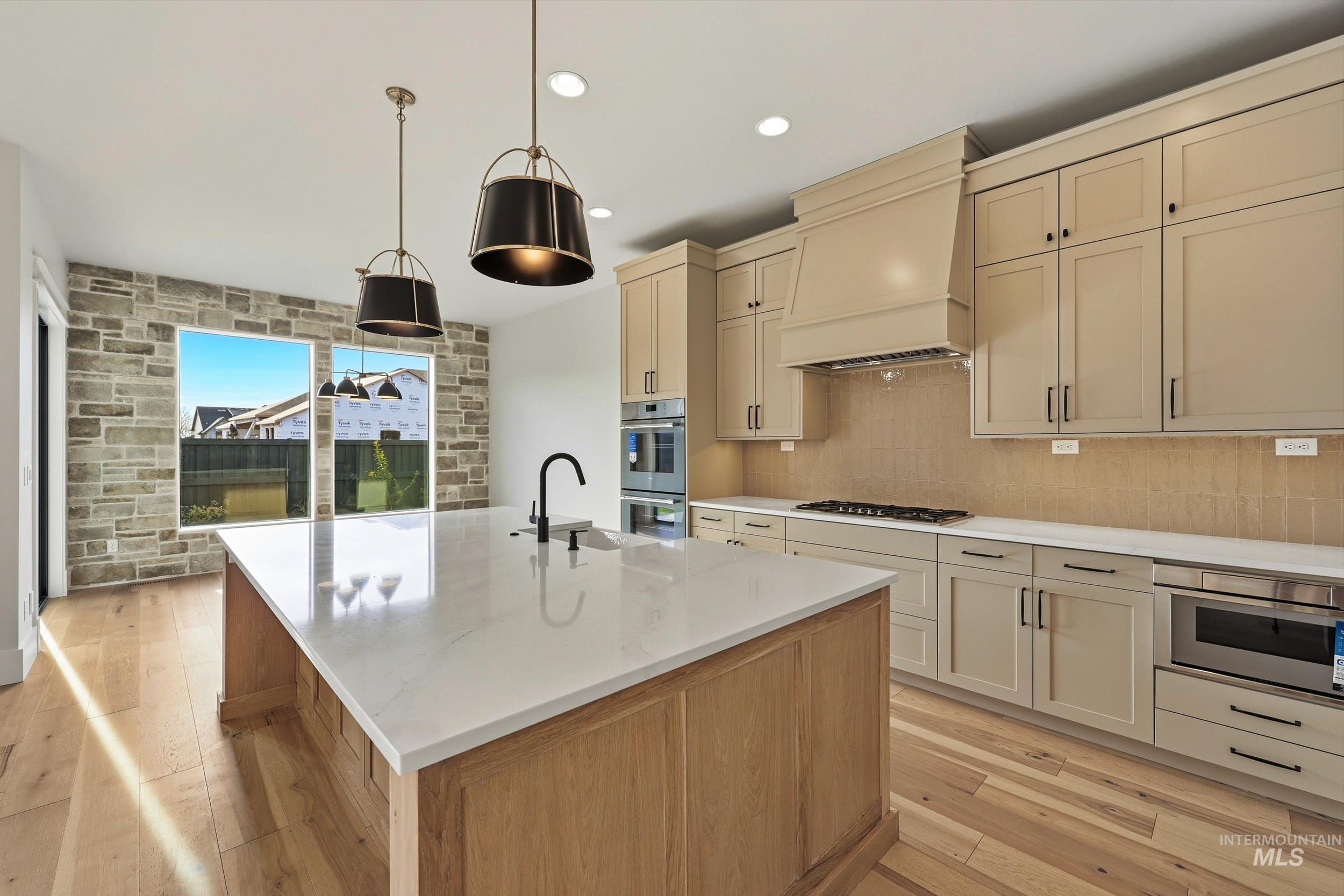 1090 East Crescendo Street Meridian, ID 83642 - Photo 7 of 43 Kitchen featuring cream cabinets, light wood finished floors, light stone counters, a center island with sink, and custom exhaust hood