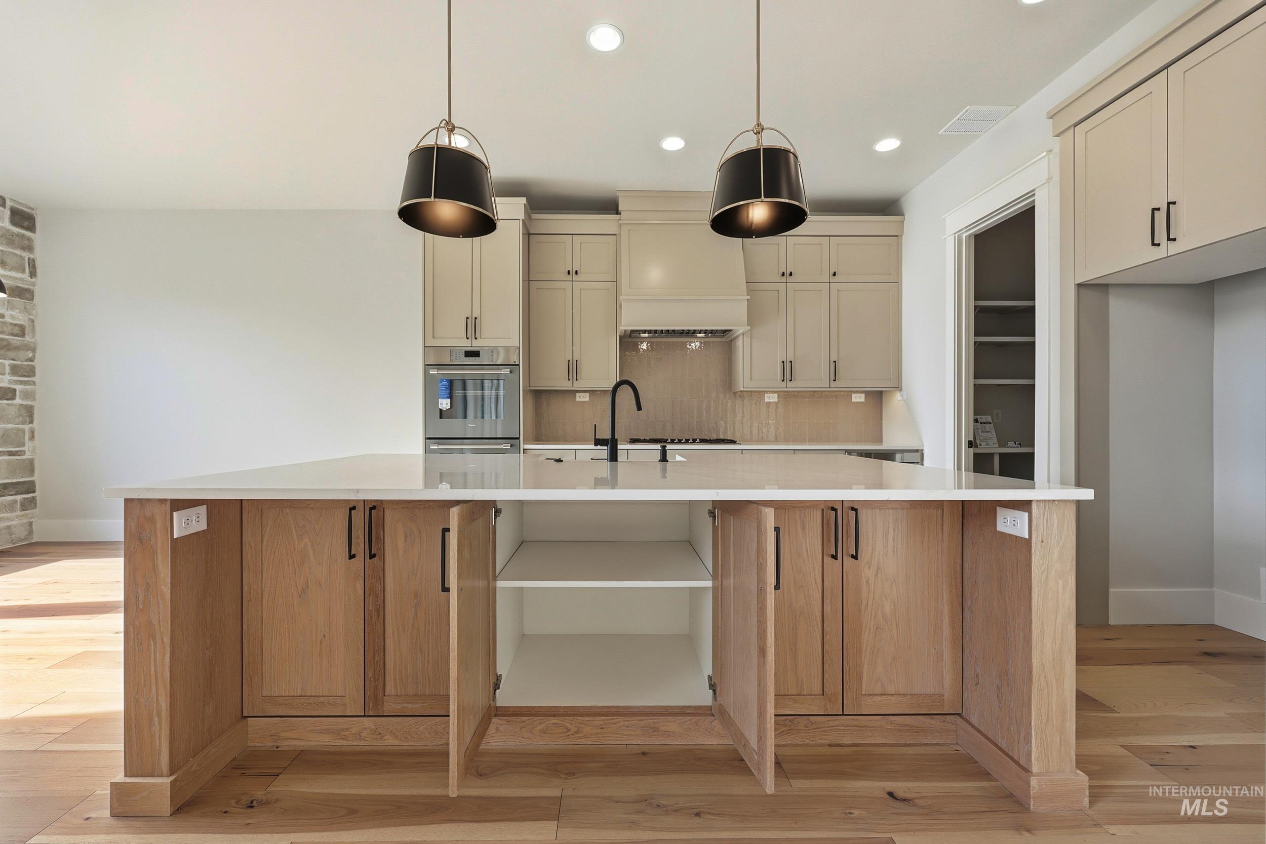 1090 East Crescendo Street Meridian, ID 83642 - Photo 10 of 43 Kitchen featuring an island with sink, decorative light fixtures, decorative backsplash, light wood-style flooring, and light stone countertops
