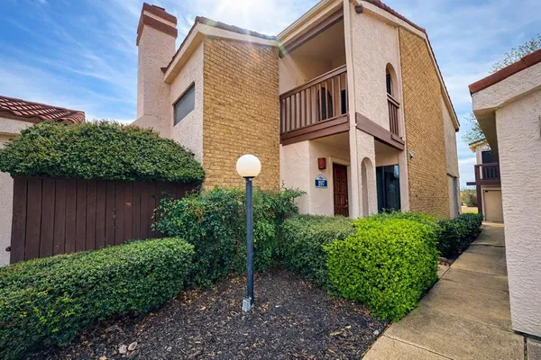 a view of a house with brick walls plants and large tree