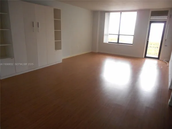an empty room with wooden floor and windows with curtains