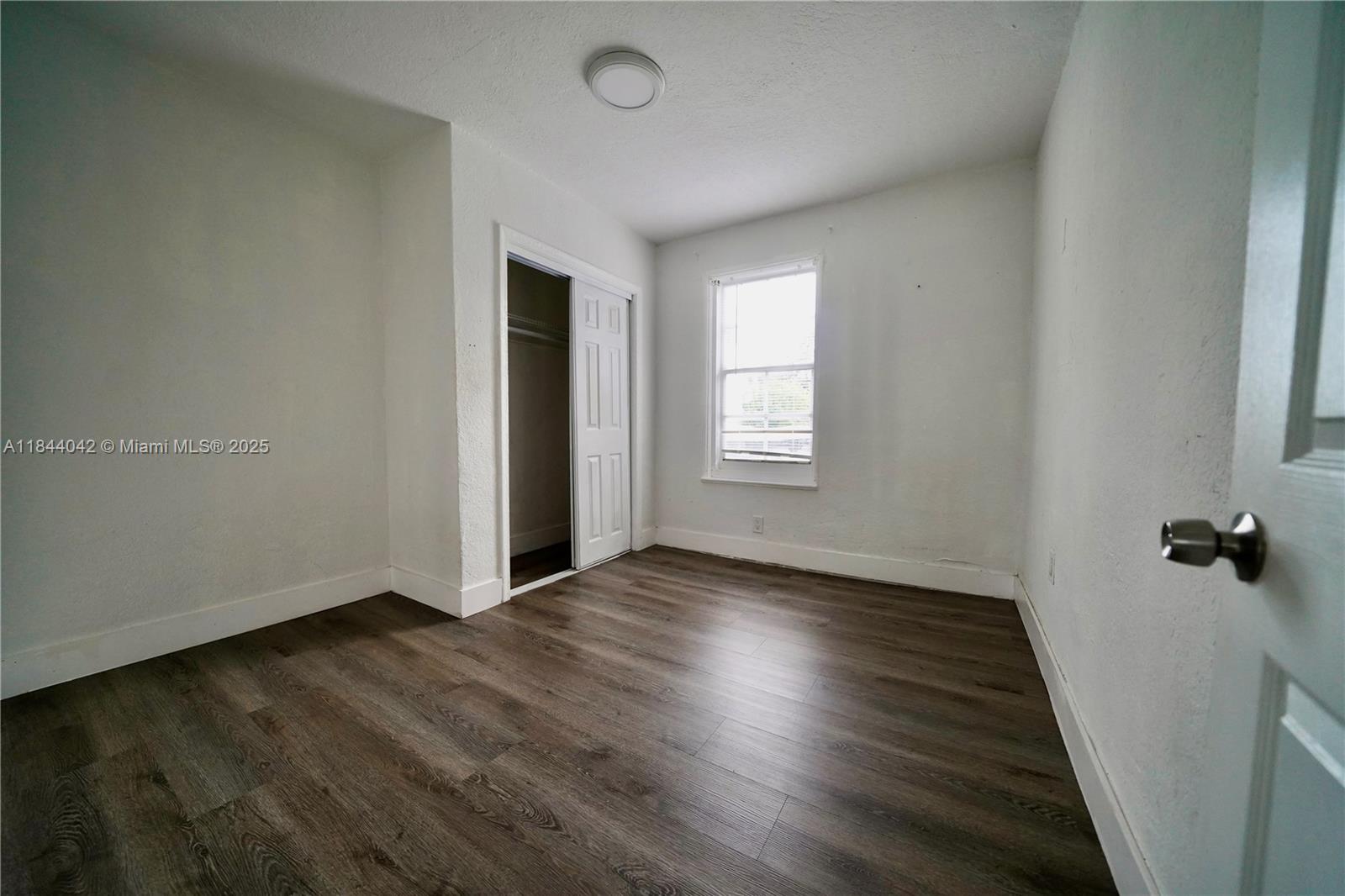 3376 Northwest 49th Street, Unit B Miami, FL 33142 - Photo 10 of 14 an empty room with wooden floor and windows