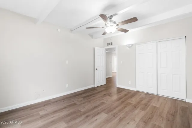 an empty room with wooden floor fan and windows