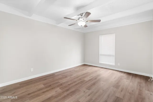 an empty room with wooden floor chandelier fan and windows