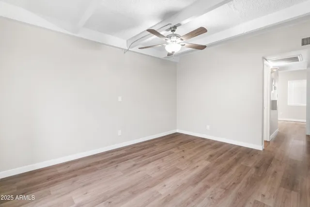 an empty room with wooden floor fan and windows