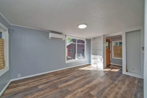 a view of an empty room with wooden floor and kitchen
