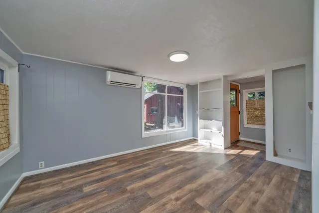 a view of an empty room with wooden floor and kitchen