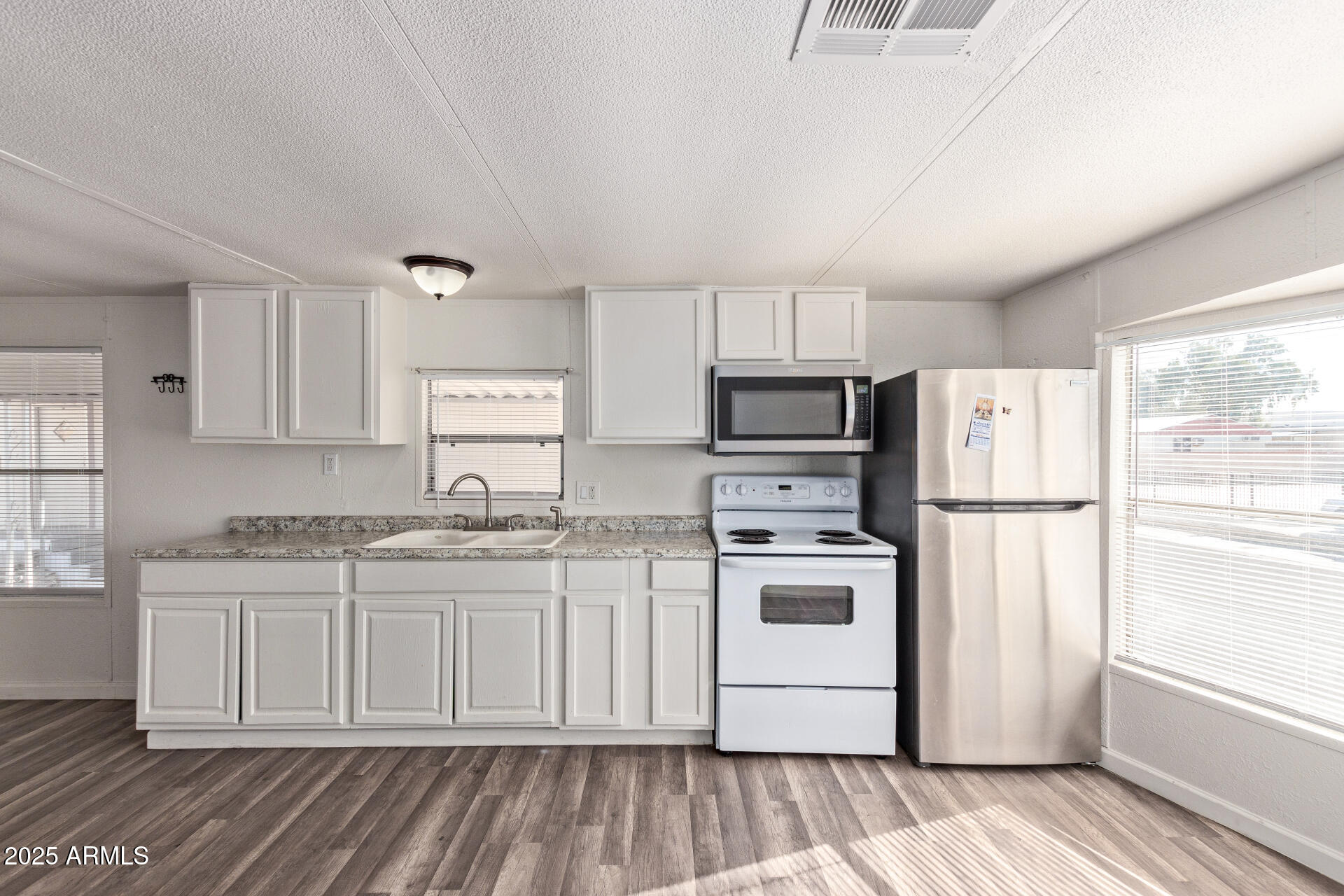 1221 North Dysart Road, Unit 35 Avondale, AZ 85323 - Photo 11 of 22 a kitchen with stainless steel appliances a refrigerator a stove a sink and white cabinets with wooden floor