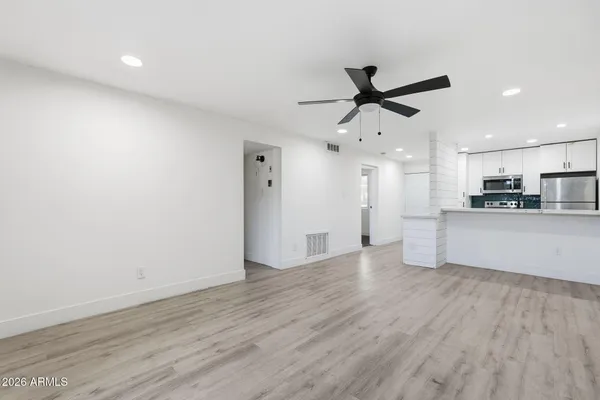 a view of an empty room with kitchen appliances and a ceiling fan