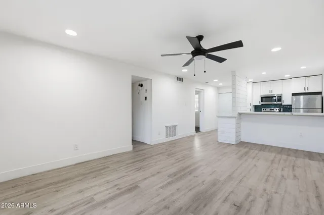 a view of an empty room with kitchen appliances and a ceiling fan