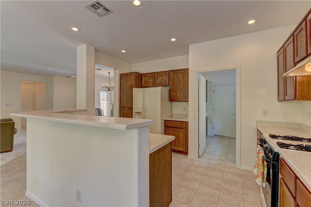 3013 Fort Stanwix Road Henderson, NV 89052 - Photo 9 of 26 Kitchen with wood finish cabinets, black gas range, white refrigerator with ice dispenser, light countertops, and light tile patterned floors