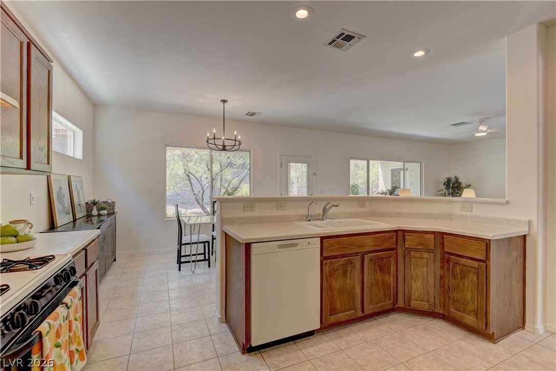 3013 Fort Stanwix Road Henderson, NV 89052 - Photo 10 of 26 Kitchen with wood finish cabinets, white dishwasher, gas stove, light countertops, and hanging lights