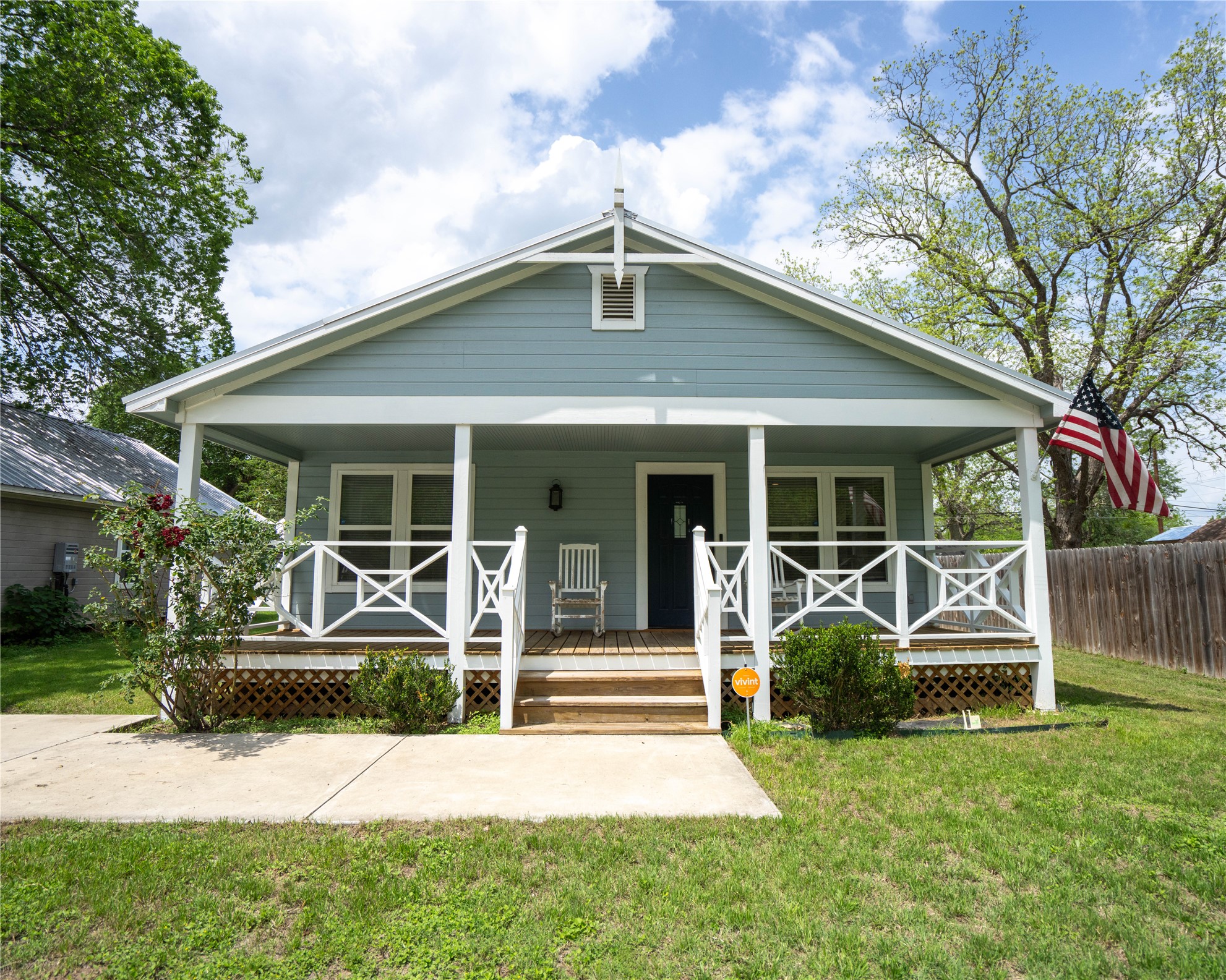 Light blue exterior siding with white trim, a covered front porch, white porch railing with decorative X-patterns, and a dark entry door