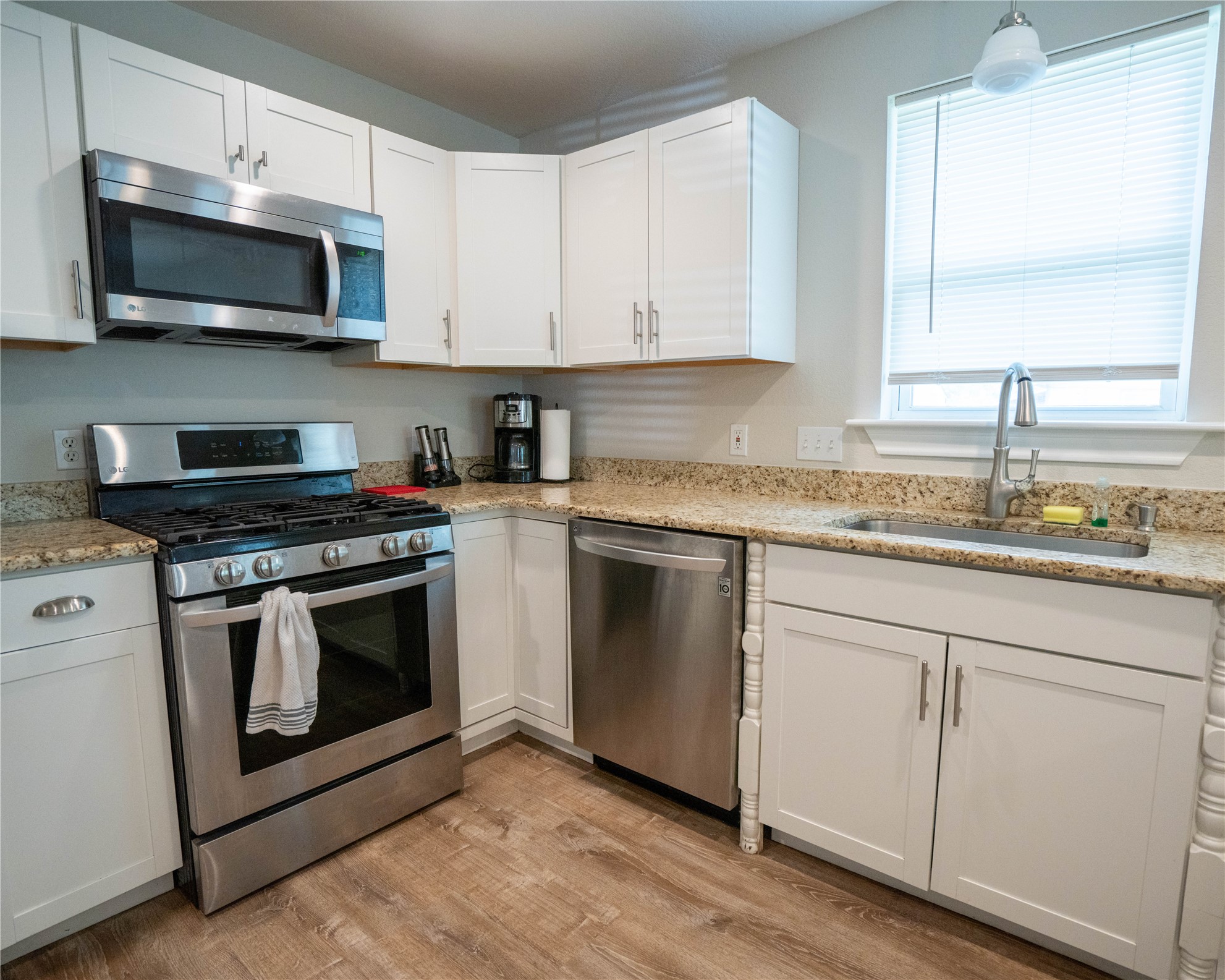 404 Rivers Street Smithville, TX 78957 - Photo 14 of 27 Kitchen featuring white shaker-style cabinetry, light-toned countertops, stainless steel appliances, a stainless steel sink with a high-arc faucet, and wood-finish flooring
