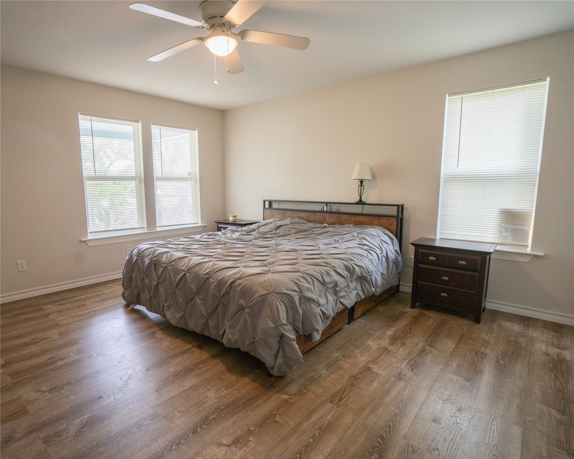 404 Rivers Street Smithville, TX 78957 - Photo 5 of 27 Spacious bedroom featuring wood-finish flooring, light neutral wall paint, a ceiling fan with integrated lighting, and multiple windows with blinds