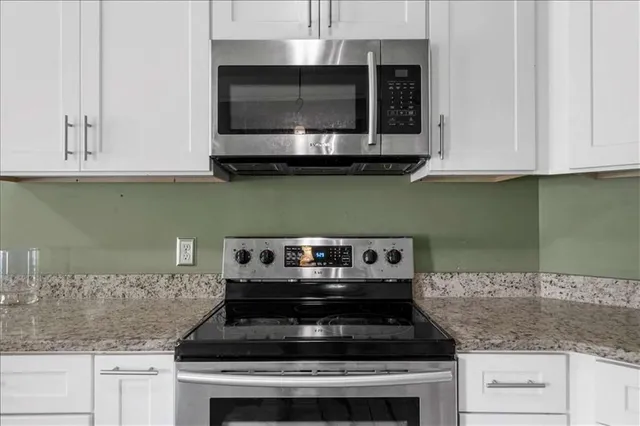 a kitchen with granite countertop white cabinets stainless steel appliances and a counter space