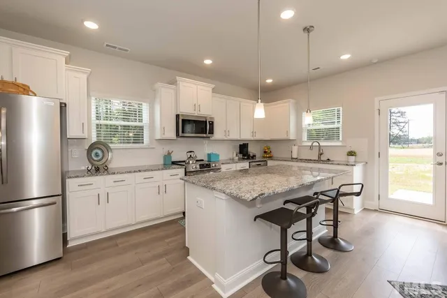 a kitchen with granite countertop a stove a sink a refrigerator and white cabinets with wooden floor