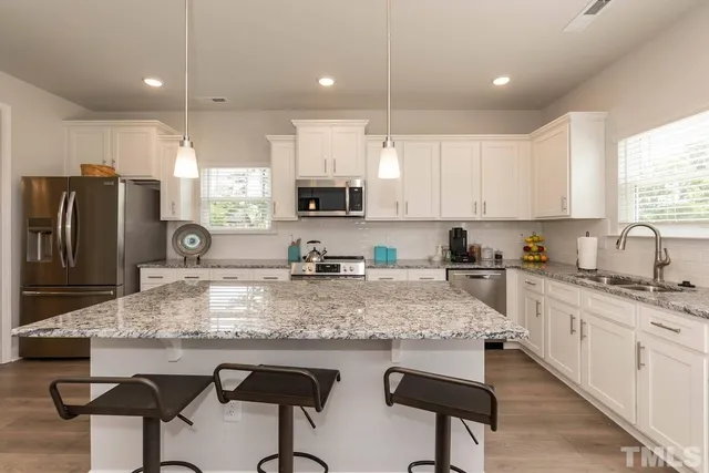 a kitchen with stainless steel appliances granite countertop a sink a stove a refrigerator cabinets and chairs