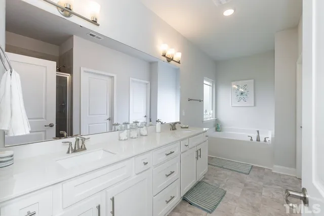 a bathroom with double vanity sinks a large mirror and a bathtub